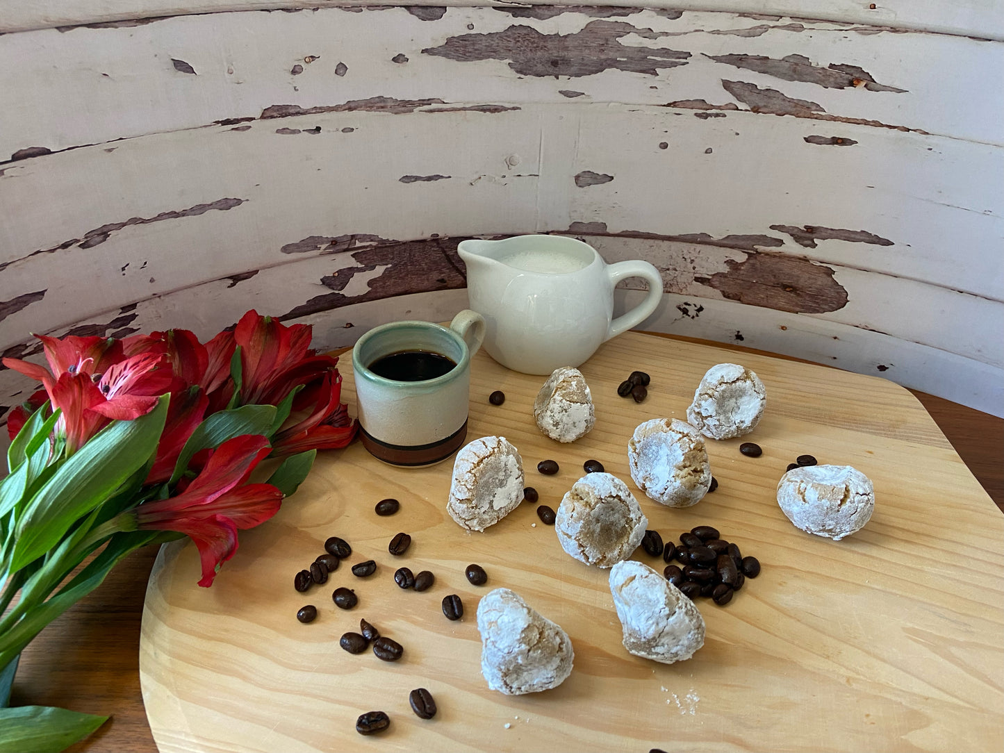 Pizzicotti Coffee: soft almond-coffe cookies on a table along with coffee beans, a cup of coffee, a cup of milk and flowers on the side