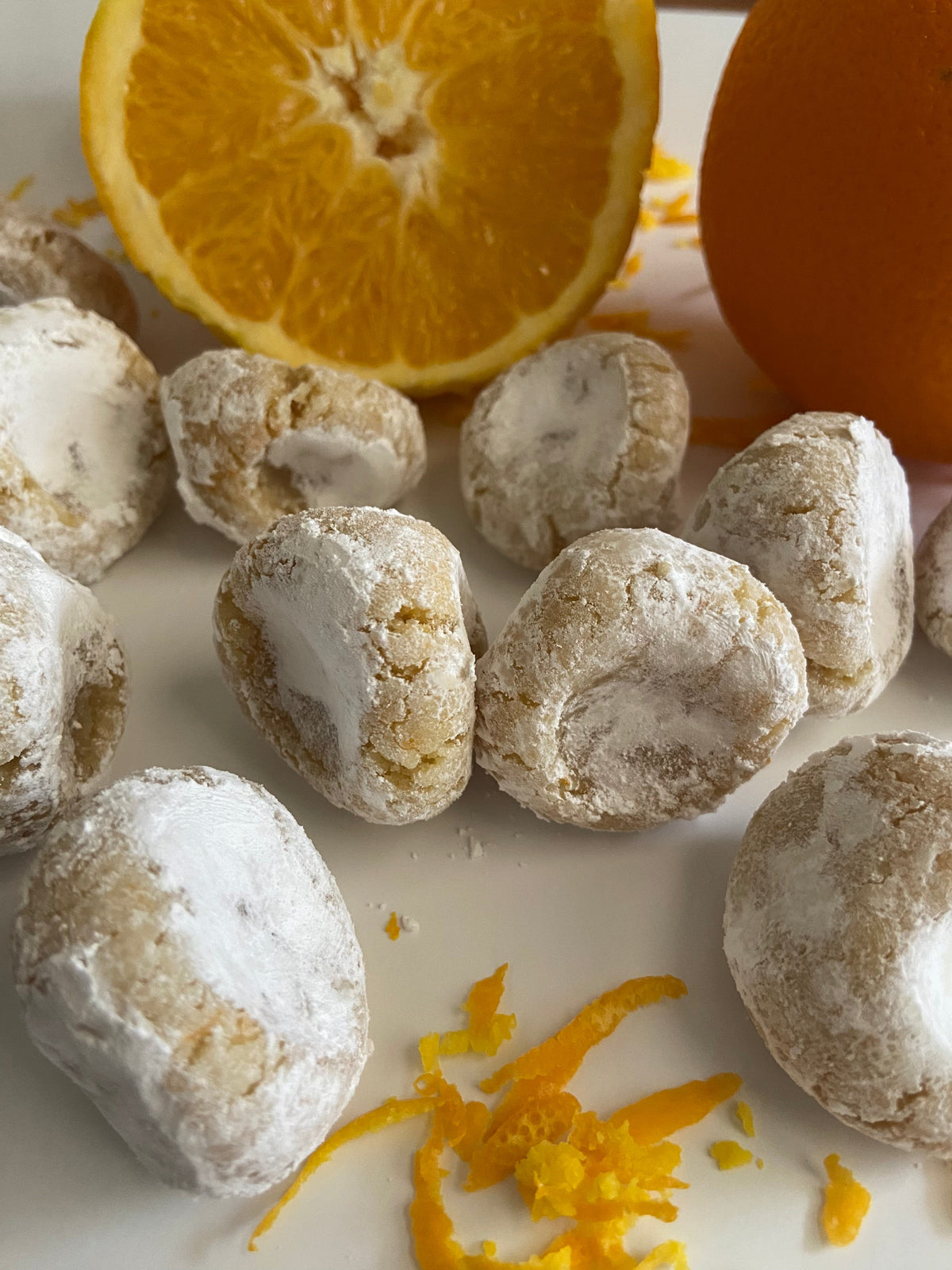 Pizzicotti Orange: Soft almond cookies along with an orange cut in half over a white background