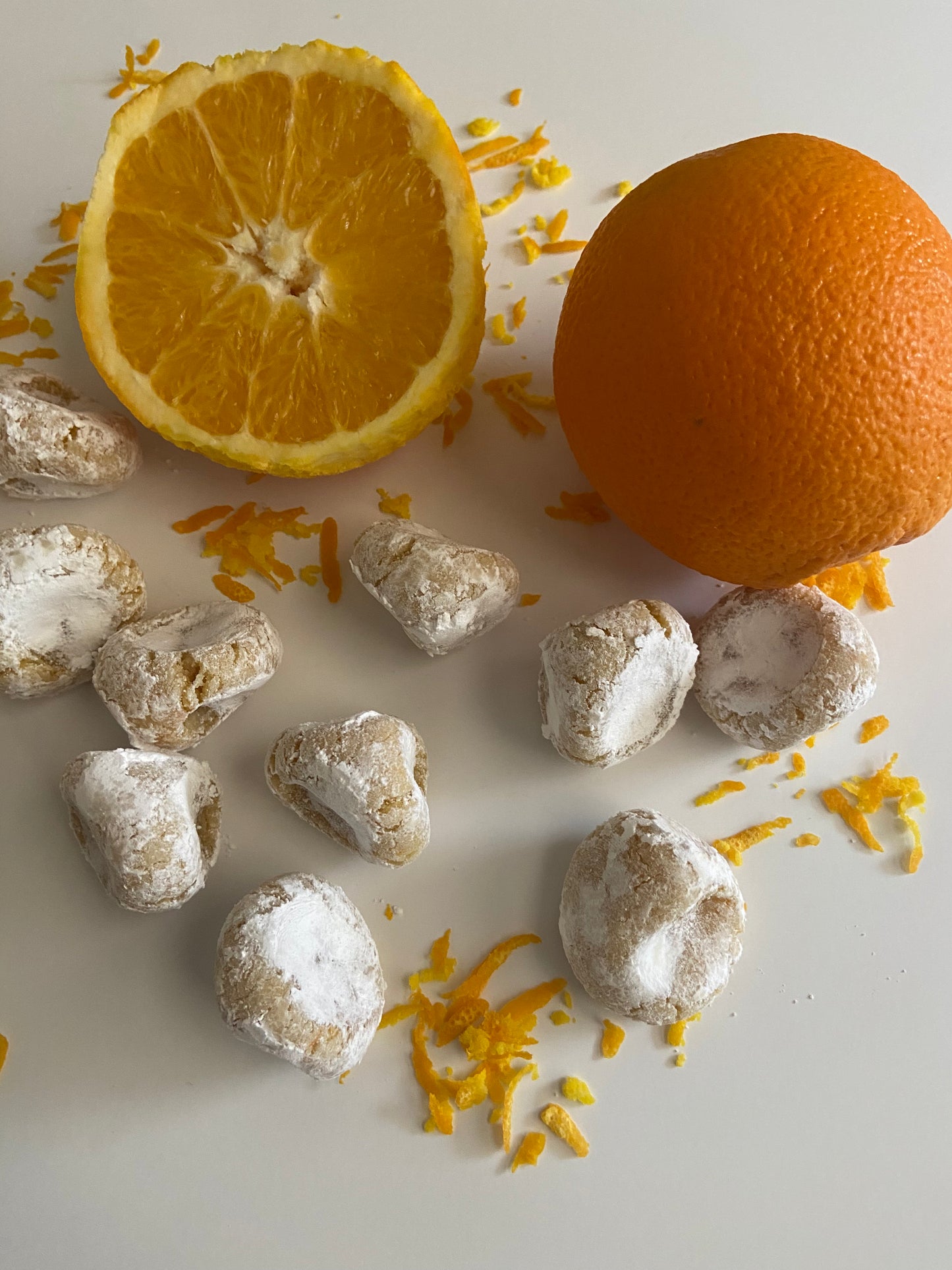 Pizzicotti Orange: Soft almond cookies along with an orange cut in half over a white background