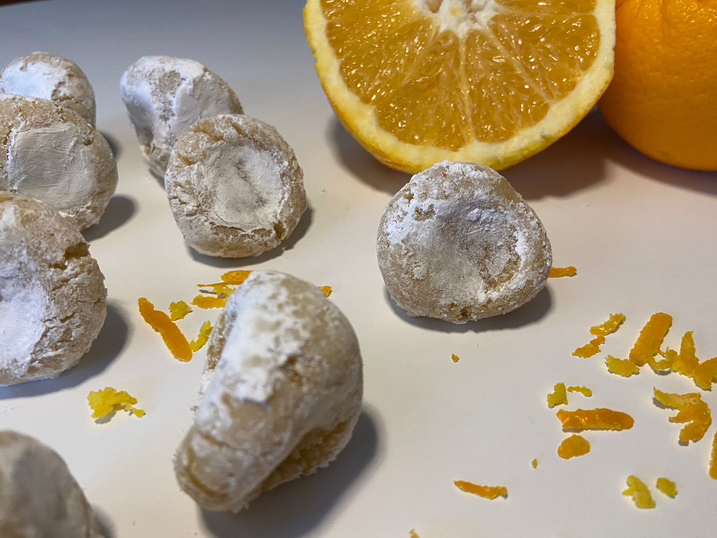 Pizzicotti Orange: Soft almond cookies along with an orange cut in half over a white background